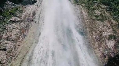 Immersive upward view of magnificent waterfall tumbling down steep rocky cliffs with bright blue sky