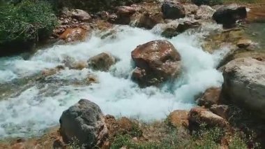 Wide shot of turquoise river flowing through rocky hilly landscape with lush green vegetation