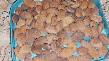 Small Metallic Container of Shelled Almonds and Apricot Kernels Inside Woven Tray Filled with Broken Nut Shells