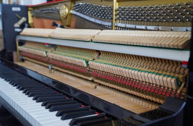 Akort işlemi sırasında siyah dik bir piyanonun yakın plan görüntüsü. Piyano kapağı açık, tellerin, çekiçlerin ve ses panosunun karmaşık detaylarını ortaya çıkarıyor.. 