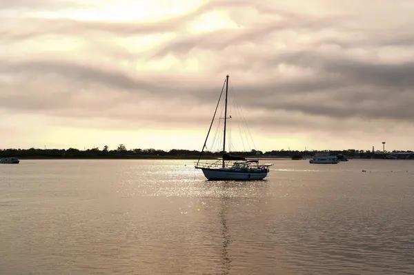 stock image A tranquil scene of a boat anchored on the water as the golden hues of the sunrise filter through the clouds. Warm glow across the sky and water. Atmosphere in the early morning light.