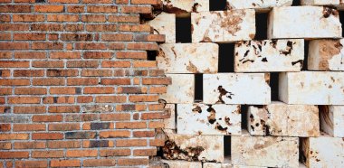 Yıpranmış bej kireç taşı blok duvarlar arka planda delikler, kir ve yosun yetişiyor. Birbirinin üzerine yığılmış bu taşlar terk edilmiş bir binadan arta kalan taşlardır..