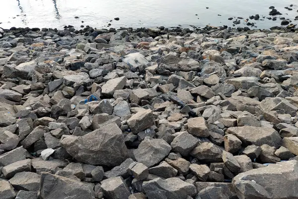 stock image Piles of basecourse rock comprised of cut grey siltstones and cobblestones, showing a construction boat and a landfill process of making several reclamation island at the background