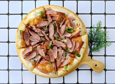 Italian pizza with cheese crest, Bolognese paste, paprika or bell pepper, cut pork sausages and herbs, with some pine nuts accessories on a white mozaic tiles table. clipart