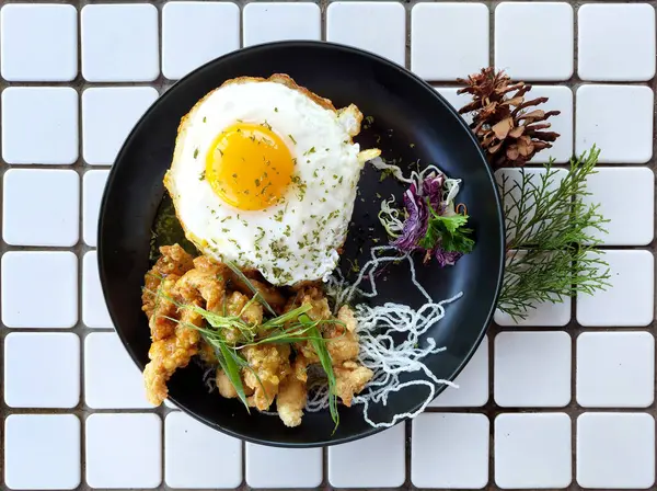 stock image Deep fried honey chicken lemon with seasoned rice, and sunny sided egg, and fresh salad with some salad dressing and sliced red purple cabbage. Served on a wooden table background. On a white mozaic tiles table.