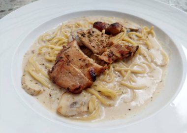 Alfredo soslu spagetti tavuğu gri terrazzo masasının üstünde makarna tabağında servis edilir. Yer mantarı, zeytinyağı, parmesan peyniri ve İtalyan otlarıyla servis edilen kremalı mantarlı tavuk..