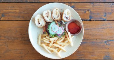 Tavuk Cordon Bleu, bezelye ve mısır salatasıyla servis ediliyor. Yanında patates kızartması ve acılı sos, ahşap bir masa üzerinde.