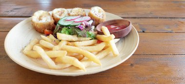 Tavuk Cordon Bleu, bezelye ve mısır salatasıyla servis ediliyor. Yanında patates kızartması ve acılı sos, ahşap bir masa üzerinde.