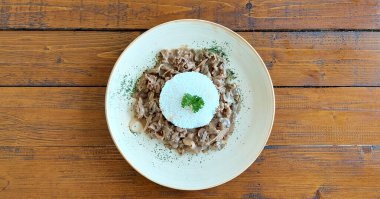 Şampiyon mantarlı kıyma ve kremalı peynir soslu beyaz glütensiz pirinç, ahşap bir sade masada servis edilir..