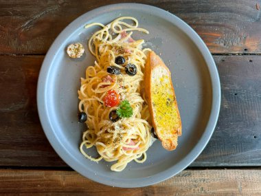 Zeytinli spagetti, bebek domatesli, maydanoz, kekik ve biberiye yapraklı sarımsaklı ekmekle servis edilen, ahşap bir sade masada servis edilen Aglio ve Olio..