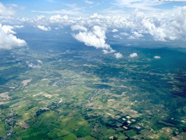 Yukarıdan, verimli toprağı, çeltik tarlalarını, dağları, dağları ve bulutları gören uçağın penceresinden nefes kesici bir hava manzarası. Ufuk çizgisinde.
