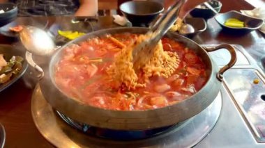 Bir el yapımı budae jjigae ya da ordu üssü yahnisi, Güney Kore yemeği, sıcak bir tencerede. Burada eriştelerin pişirildiğini görüyoruz, güveçten duman buharı yükseliyor, biraz gochujang ezmesiyle..