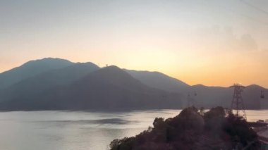 Hong Kong, Lantau Adası 'ndaki Ngong Ping 360 teleferiğinin nefes kesici görüntüsü. Günbatımı gökyüzünde çekilmiş bir video. Teleferikle ünlü tepeleri ve kırsal bölgeleri yukarıdan gören.