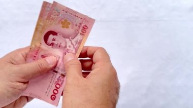 Tayland Baht 'ı 100 Baht' ta sayarken 4K el ve parmak görüntüsü. Tayland Baht banknotlarını sayan eller beyaz arkaplanda izole.