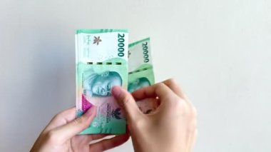 Endonezya Rupiah 'ının Rp20.000 nominal değerindeki el ve parmak sayımının 4K görüntüsü. Beyaz arka planda izole edilmiş IDR 20K banknotlarını sayan eller.