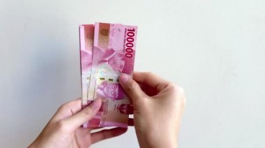 Endonezya Rupiah 'ının Rp100.000' deki el ve parmak sayımının 4K görüntüsü. Beyaz duvar zemininde izole edilmiş IDR 100 bin banknot sayan eller.