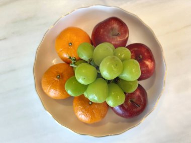 Yeşil üzümlerden, elmalardan ve portakallardan oluşan bir kase beyaz mermer bir masada izole edilmiş..