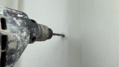 4K görüntü, marangozluk katı duvarın içinde vida ve duvar tıkaçları için delik açmaya çalışıyor. Marangozluk kurulum sürecinin bir parçası olarak beyaz bir duvarda delik açan elektrikli matkapları kapatın.
