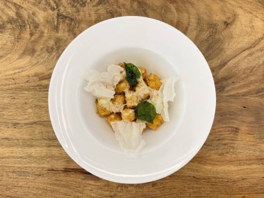 Kızarmış patates püresi kahverengi rendelenmiş ve mozzarella peyniri, kızarmış ıspanak yaprağı ve kraker ile birlikte beyaz tabakta kırmızı sos sosu. Ahşap kırsal masada servis edilir..