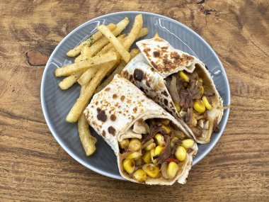 Klasik Meksika Burrito 'suna yakın. Gri tabakta servis edilen patates kızartması, ahşap bir kırsal masada..