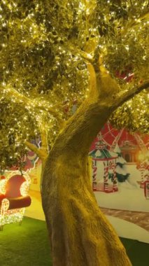 Işıklı, pırıl pırıl ışık ve buz saçağı ışıklarıyla altın ağaçtan 4K görüntü. Noel 'i, Noel' i ve yeni yılı kutlamak için ışıklarla süslenmiş büyük bir ağaç. İyi geceler..
