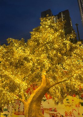 Golden tree leaves with LED twinkle lights or icicle lights. Big gold tree decorated with yellow lights to celebrate seasons greetings, holiday season of Christmas and new year. Night shot. clipart