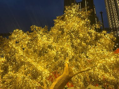 Golden tree leaves with LED twinkle lights or icicle lights. Big gold tree decorated with yellow lights to celebrate seasons greetings, holiday season of Christmas and new year. Night shot. clipart