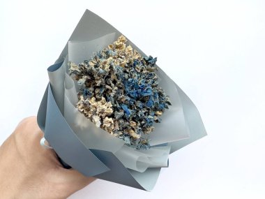 Kurumuş yapraklar ve kağıttan yapılmış mavi kağıt çiçek buketi mavi ve bej rengine boyanmış. Mavi kağıda sarılı çiçek buketi, kadınsı ve kadınsı bir aşk. Beyaz arkaplanda izole.