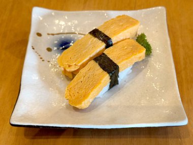 Tamago suşisini deniz yosunu ya da nori ve porselen tabakta geleneksel Japon pirinci ile kapat..