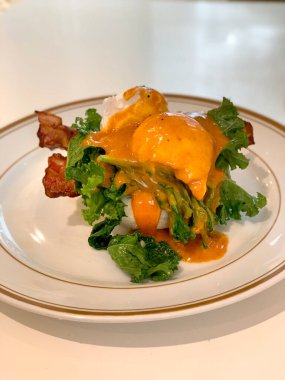 Kızarmış domuz pastırması, marul ve haşlanmış yumurta, beyaz bir tabakta, beyaz bir masada servis edilir..