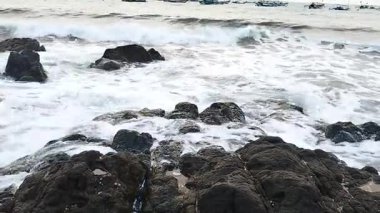 Okyanus dalgalarının sahile vuran kayaları görüntüsü. Deniz kıyısındaki çakıl taşlarına su sıçrayan dalgalar, sahil kıyıları. Temiz su, yüksek gelgit dalgası. Doğa görünümü.