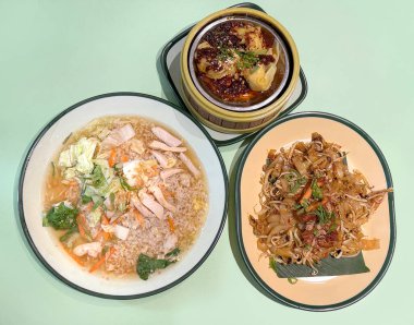 Bir dizi Çin yemeği ve gamzesi. Tavuklu kızarmış şehriye, tavuklu sebzeli sebze çorbası ve yeşil masa arkasına izole edilmiş acılı tavuk çorbası..