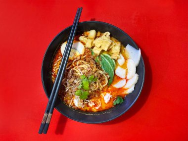 Yumurta ve sebzeli deniz ürünleri ve karidesli laksa eriştesi. Laksa, Güneydoğu Asya, Singapur, Endonezya ve Malezya 'da bulunan ünlü bir Çin mutfağıdır. Kırmızı masa arkaplanında servis edildi.