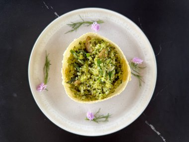 Yeşil acılı tavuk baharatlı pilav ile yenilebilir çiçekler, yuvarlak şekilli kızarmış wonton derisi ile servis ve siyah bir masada beyaz bir tabakta servis.