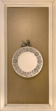 Klasik kalıp çerçeveli kahverengi bir duvara asılmış dantelli ve kurdeleli süs tabakasını kapat. Koloni kalıtımsal plakası.