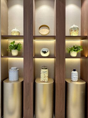 İç dekoratif aksesuarlar serisi modern bir vitrinde sergileniyor, ahşap paneller ve metalik altın boyayla yapılmış. Lüks ve zarif iç tasarım.