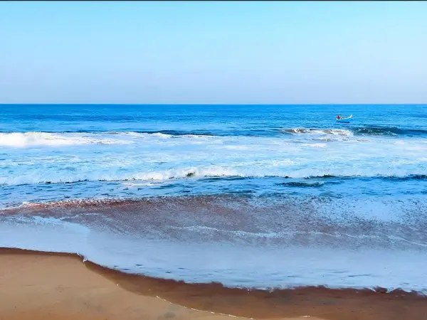 Okyanus dalgalarının parlak mavi gökyüzünün altında ufukta görünen uzak bir tekneyle kumlu sahile gelişinin büyüleyici bir görüntüsü..