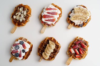 Bir grup dekore edilmiş kruvasan waffle veya karamel, çikolata sosu, muz dilimleri, çilek, yabanmersini, badem ve krem şantili krema..