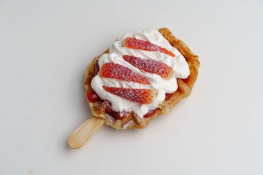 Üstünde çilek ve krema olan bir tatlı. Tatlı çubukta servis edilir. Tatlı lezzetli ve davetkar görünüyor.