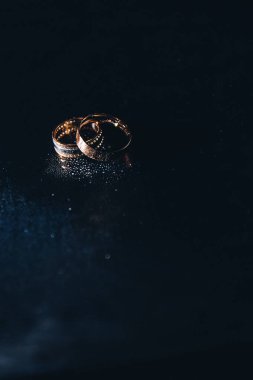 İpek kumaş üzerinde iki zarif alyans yakın plan. Elmaslarla işlenmiş altın yüzükler zarif ve lüks olduklarını vurgulayarak yumuşak bir ışıkta parlıyor. Düğün, nişan ve aşk temalarını tasvir etmek için mükemmel