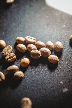 Fotoğraf koyu bir arka planda birkaç kahve çekirdeğini gösteriyor. Kahve çekirdeklerinden biri ön planda yer alır, açıkça onun dokusuna ve detaylarına dikkat çekerken, diğer fasulyeler ise bir aydınlatmaya yerleştirilir.