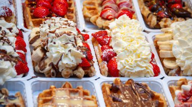 Krema, süt ve çikolatayla kaplanmış çeşitli waffle çeşitlerini beyaz plastik tepside sıralanmış çilek ve muzlu hamur işleri gibi çeşitli meyvelerle görüntüle