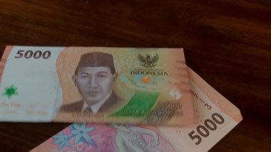 Rupiah banknotları ahşap bir masaya düşüyor. 5000 rupi, Endonezya parası.