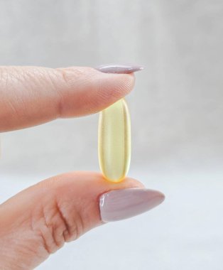 Parlak omega 3 tabletini yücelten parmaklar. 