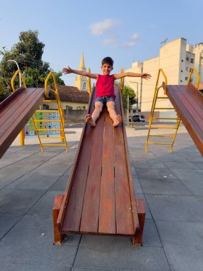 Child having fun on the slide in a public square in the late afternoon clipart