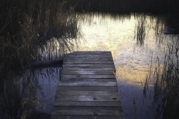 Günbatımında gölün kıyısındaki ahşap köprü, ormanda, akşam güneş ışınları, suya yansıyan yapay zeka.