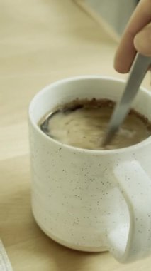 Tahta bir masanın üzerine çay kaşığıyla yerleştirilmiş beyaz bir fincan kahve. 