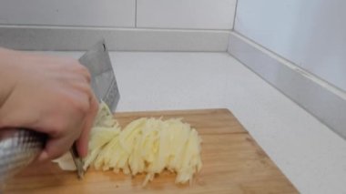 Patates dilimlerini mutfak bıçağıyla dilimlemek ahşap kesim tahtasında. Aşçı elleri, kızartma tabakları için mutfak bıçağıyla çiğ patatesi dilimliyor. Yakın çekim, yavaş çekim..
