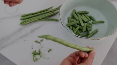 Eller hünerli bir şekilde akşam yemeği için taze yeşil fasulye katlar, tabakları kızartma için hazırlar. Yeşil fasulye saplarını elle soyarlar..