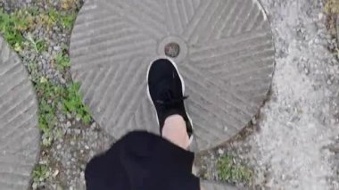 POV üst görüş bacağı siyah spor ayakkabılarla siyah eteğin altında kaldırıma basarak yaz aylarında taşlarla ve yulaflarla. Yürüyüş ve egzersiz konsepti. İlk adım atma görüntüsü.
